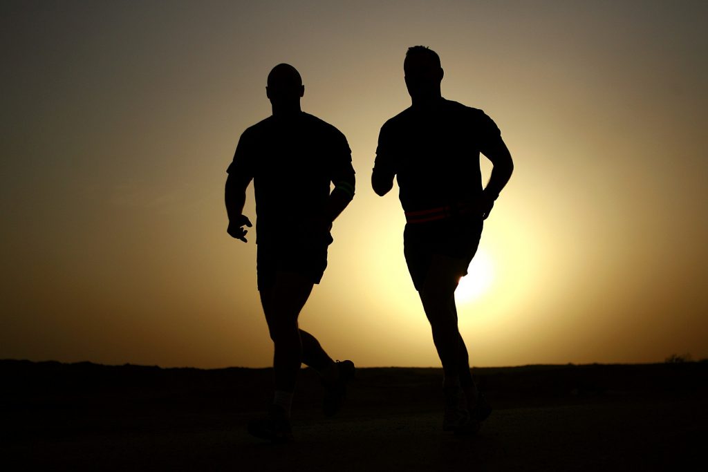 Silhouettes of two men running together at sunset with a vibrant sky in the background
