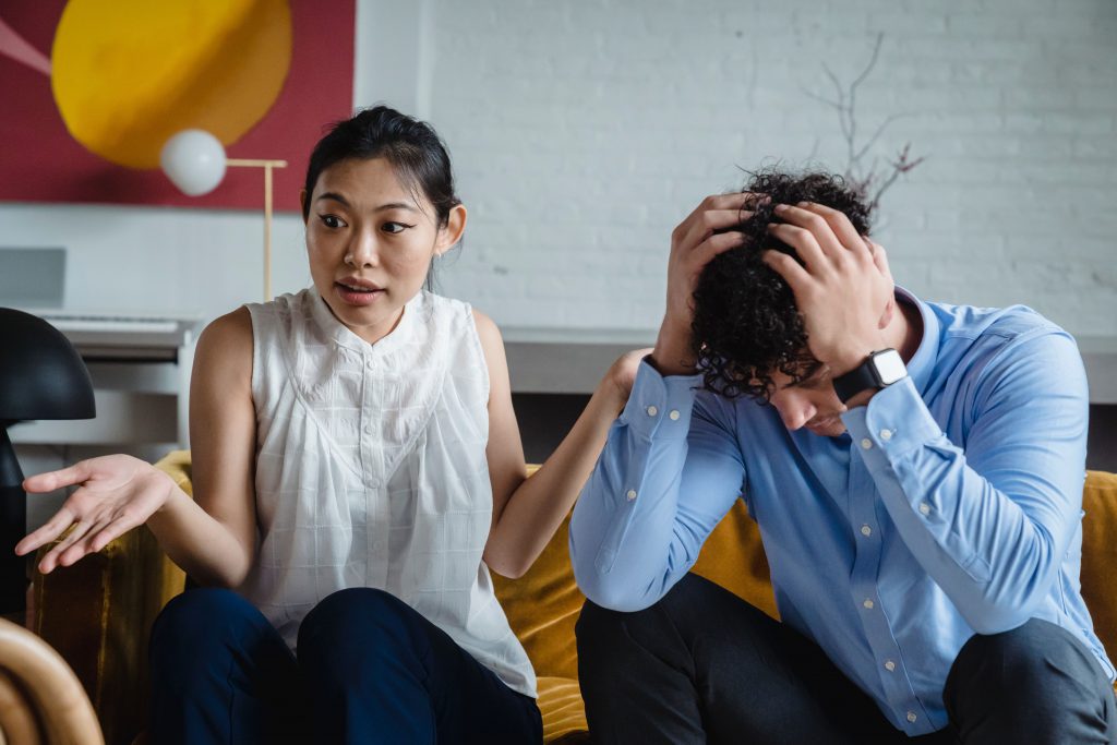 Stressed couple sitting on a couch with hands on their heads, appearing overwhelmed and distant